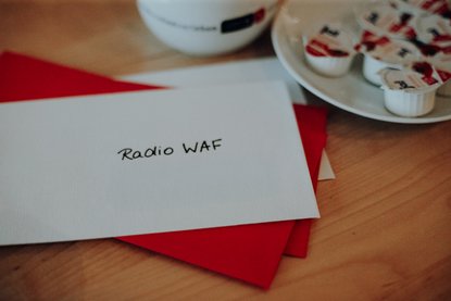 Weißer Briefumschlag, der als Adresse Radio WAF trägt, auf einem roten Umschlag, beide liegen auf einem Tisch
