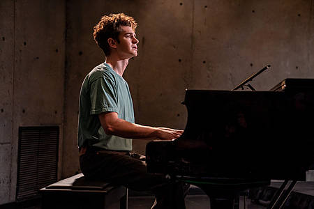 Andrew Garfield sitzt an einem Piano. 