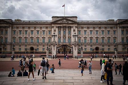 Touristen stehen vor den Toren vom Buckingham Palast in London.