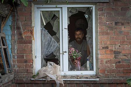 Ein Mann in Bachmut stellt in seinem durch russischen Beschuss beschädigten Haus Blumen  auf die Fensterbank.
